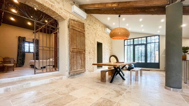 Una habitación amplia con pared de piedra, puerta de madera, ventana grande y comedor con mesa y sillas.