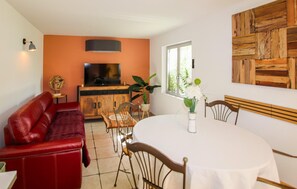 A living room with a red sofa, a TV, a wooden cabinet, a dining table with chairs, and a window with plants. - Awesome home in Courthezon with WiFi (Courthezon)