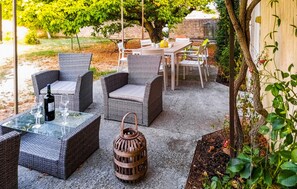 Un patio al aire libre con muebles de mimbre, una mesa de vidrio con una botella y vasos, y un farol.