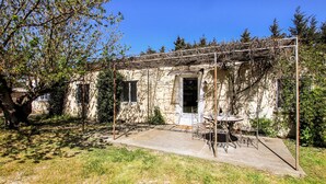 Un bâtiment rustique en pierre, doté d’un patio couvert, d’une porte et d’une petite table avec des chaises.