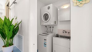 A compact laundry area with a washing machine, dryer, and sink, including energy and water saving labels. - Ocean Breeze Unit 10, 42 King Street, Kings Beach (Kings Beach)