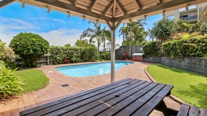 A backyard with a swimming pool, a wooden deck, and a covered seating area. - Ocean Breeze Unit 10, 42 King Street, Kings Beach (Kings Beach)