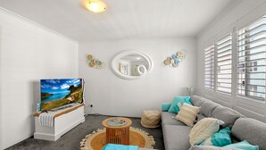 A modern living room with a flat-screen TV, a sofa, a round coffee table, and a decorative mirror. - Ocean Breeze Unit 10, 42 King Street, Kings Beach (Kings Beach)