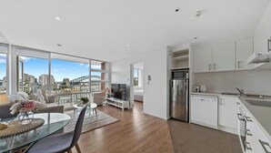A modern apartment with a balcony, a kitchen, and a dining area with a view of the city. - KozyGuru | Iconic Panorama | Harbour Front Living (Lavender Bay)