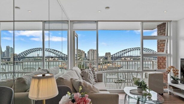 A spacious living room with large windows offering a view of the Sydney Harbour Bridge. - KozyGuru | Iconic Panorama | Harbour Front Living (Lavender Bay)