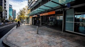A modern building with a glass facade, a clear sign for 'North Sydney,' and a pedestrian area with a stone pavement. - KozyGuru | Iconic Panorama | Harbour Front Living (Lavender Bay)