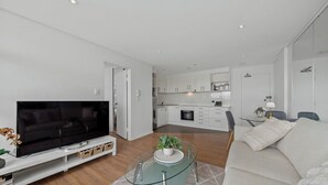 A modern living room with a flat-screen TV, a glass coffee table, and a sofa. - KozyGuru | Iconic Panorama | Harbour Front Living (Lavender Bay)