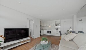 A modern living room with a flat-screen TV, a glass coffee table, and a sofa.