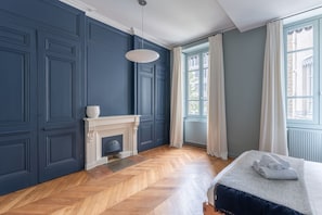 Una habitación con chimenea, una cama, un ventanal con cortinas y suelo con diseño de espiga.