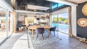 A modern dining area with a round table, chairs, and a view of a swimming pool. - Villa Mindoya - Villa pour 10, piscine chauffée (Labenne)
