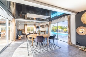 A modern dining area with a round table, chairs, and a view of a swimming pool. - Villa Mindoya - Villa pour 10, piscine chauffée (Labenne)