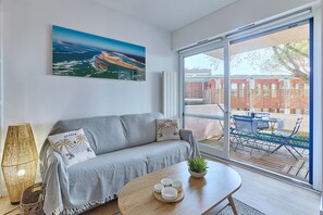 A modern living room with a grey sofa, a wooden coffee table with cups, a large window with a view of a balcony, and a painting of a landscape. - I Sen Pla - À 750m de la plage (Andernos-les-Bains)