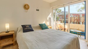 Ein Schlafzimmer mit Bett, Nachttisch, Lampe und Blick ins Freie.