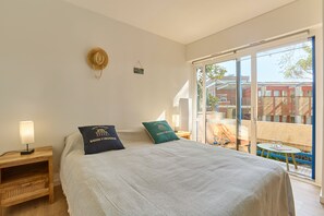 A bedroom with a bed, a nightstand, a lamp, and a view of the outside. - I Sen Pla - À 750m de la plage (Andernos-les-Bains)