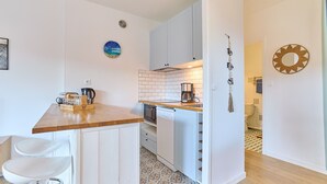 Eine kleine Küche mit weißen Schränken, einer Holz Arbeitsplatte und einer gemusterten Spritzschutzwand.