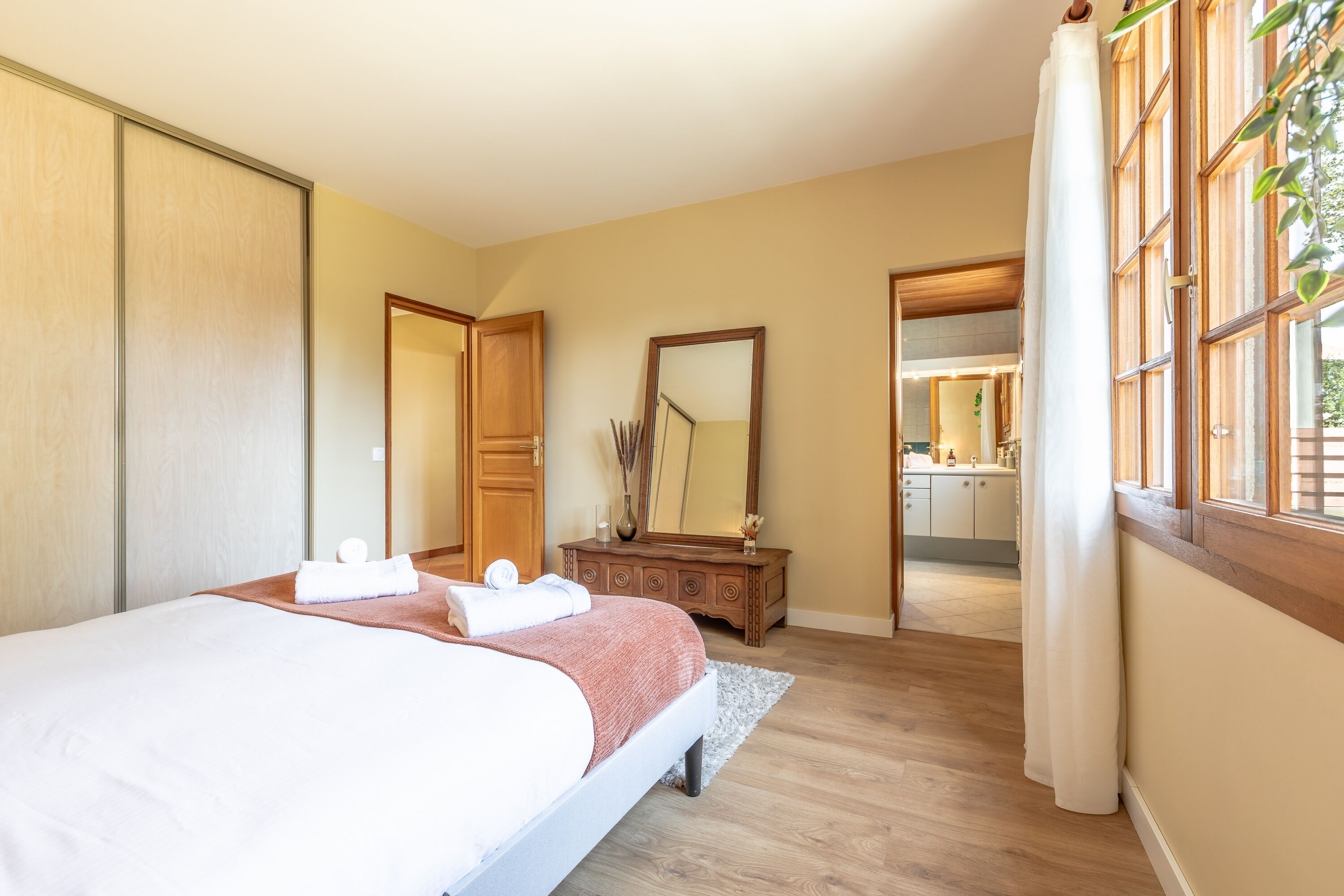 Une chambre à coucher avec un lit, une commode, un miroir et une vue sur la salle de bain.