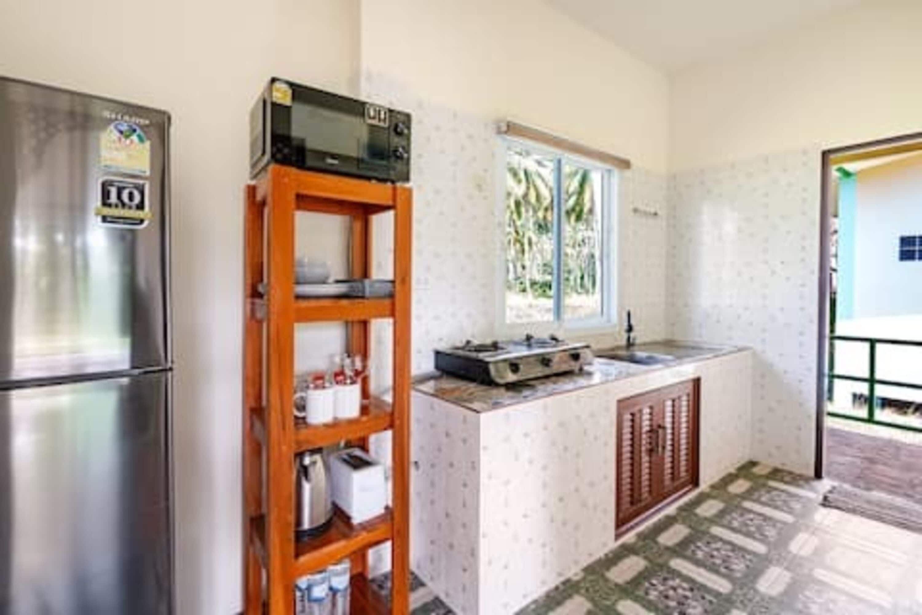 A compact kitchen with a refrigerator, a wooden shelf unit, a window, and a sink.