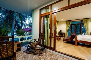 Una habitación con cama, una mecedora, un escritorio y vistas a palmeras a través de un ventanal corredero.