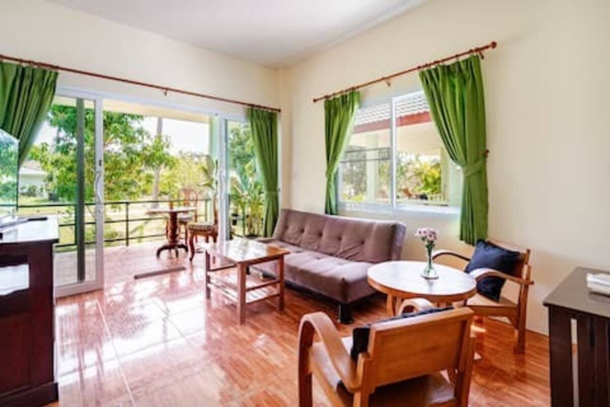 Una habitación con un sofá, una mesa redonda y una silla. Hay una ventana con cortinas.