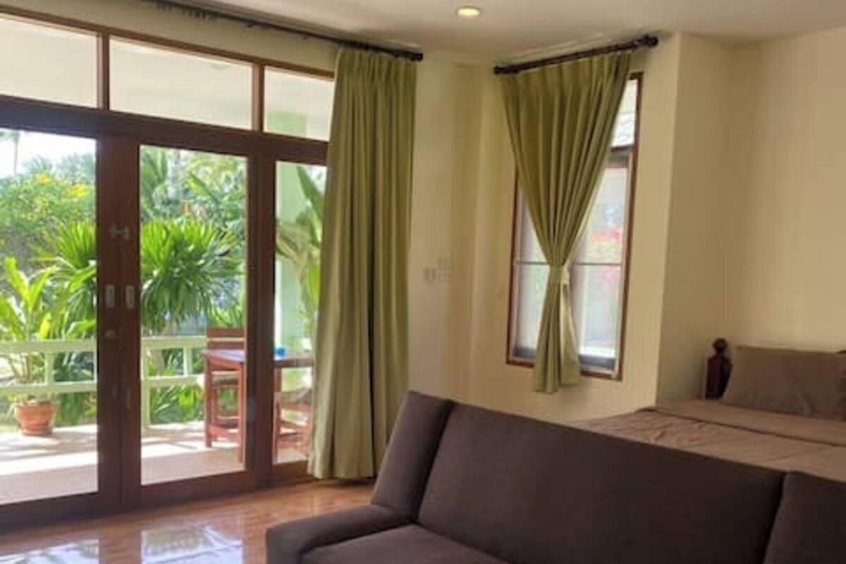 Un espacio habitable amplio con un sofá marrón oscuro, puertas correderas de vidrio que dan a un balcón y una ventana pequeña con cortinas.