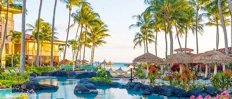A resort with a pool surrounded by palm trees and tropical plants.
