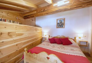 A wooden-paneled bedroom with a bed, pillows, a nightstand, and a wall-mounted picture. - CASA-Marguerite centre St Véran cosy 3ch (Molines-en-Queyras)