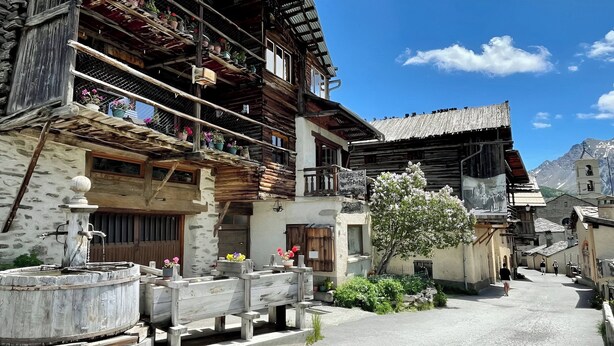 Ein traditionelles Holzhaus mit Balkonen, einer Steinmauer und Bergblick.