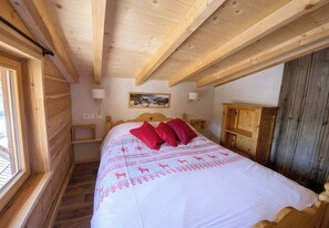 Quarto de madeira com cama, janela, luminária na parede e armário de madeira.