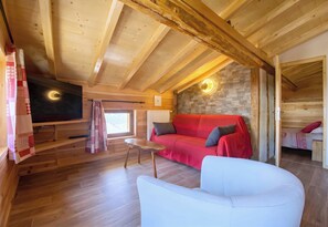 A wooden interior with a red sofa, white armchair, and a television. - CASA-Marguerite centre St Véran cosy 3ch (Molines-en-Queyras)