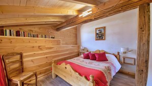 Ein Zimmer aus Holz mit einem Bett, einem Sessel, einem Bücherregal und einem Bild an der Wand.