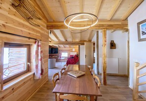 A wooden interior with a dining table, chairs, a hanging light fixture, and a view through a window. - CASA-Marguerite centre St Véran cosy 3ch (Molines-en-Queyras)