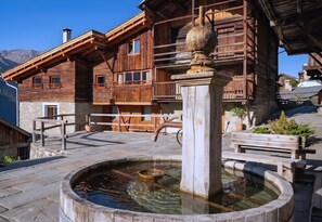 A wooden building with a stone fountain, wooden benches, and a stone pathway. - CASA-Marguerite centre St Véran cosy 3ch (Molines-en-Queyras)