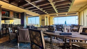 Ein Restaurant mit hohen Decken, gemusterten Sitzpolstern und großen Fenstern mit Blick.