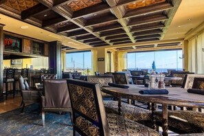 Un restaurant avec de hauts plafonds, des tissus d’ameublement à motifs et de grandes fenêtres offrant une vue panoramique.