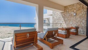 Ein Balkon mit Holzliegen, einer Steinmauer und Blick auf den Strand.