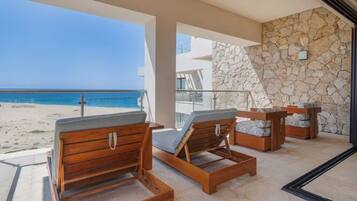 A balcony with wooden lounge chairs, a stone wall, and a view of the beach.