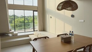 Ein Essbereich mit einem großen Tisch und Stühlen, einer Hängelampe und Blick durch große Fenster.