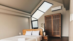 Ein Schlafzimmer mit schrägen Wänden, einem Bett, einem Nachttisch, einem Holzschrank und einer Klimaanlage.