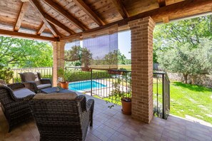 Eine überdachte Terrasse mit Korbmöbeln, einem Pool und Blick auf einen Garten.