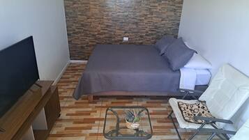 A small, neatly arranged bedroom with a bed, a TV, a chair, and a small table.