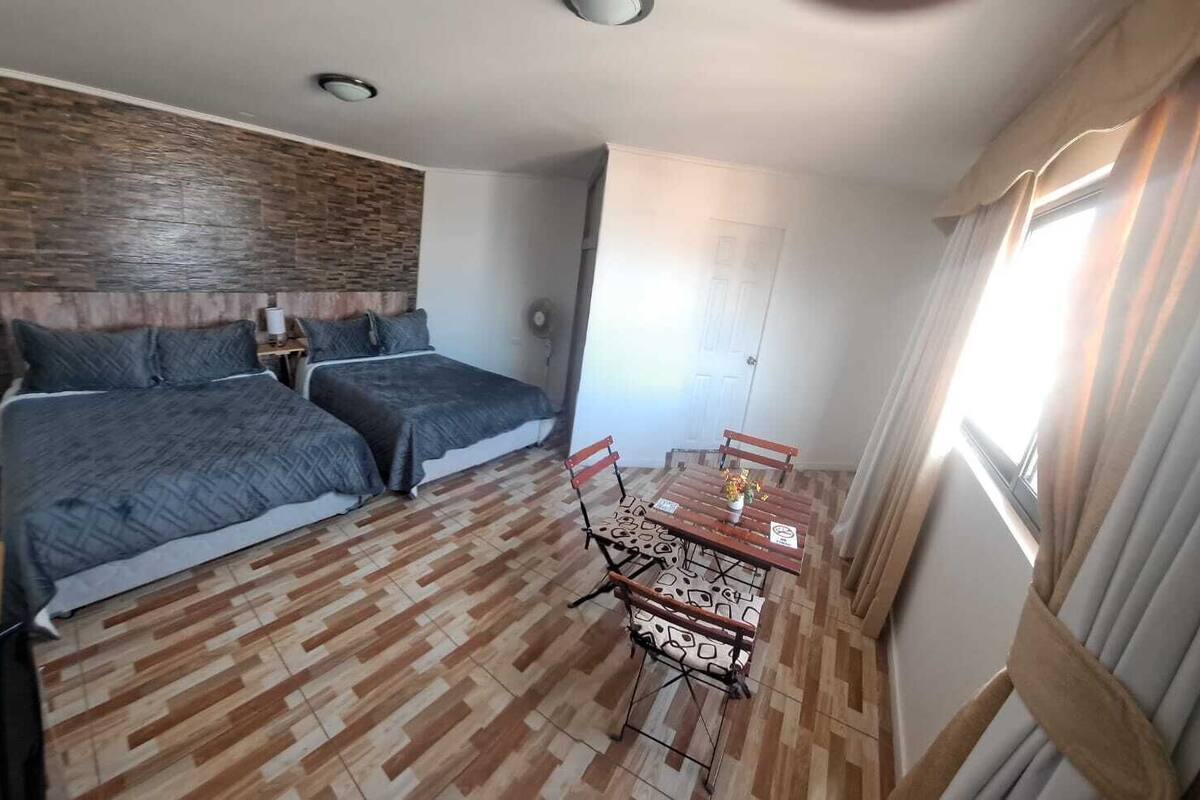 Un dormitorio con dos camas, suelo de madera, una mesa de comedor con sillas y una ventana con cortinas.
