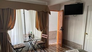 Une pièce comprenant un lit, une table avec des chaises, un téléviseur fixé au mur et une porte.