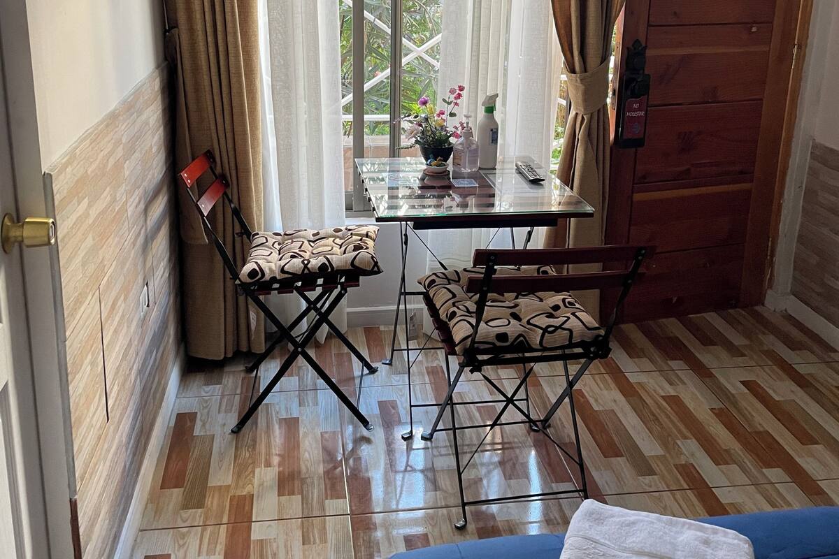 Una habitación con cama, una mesa con sillas, televisión y vista a zonas verdes.
