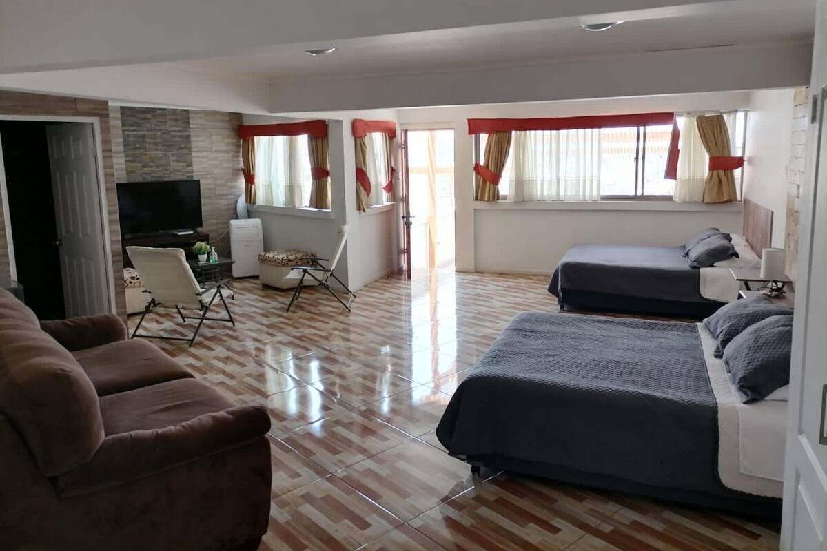 Una habitación de hotel con sofá, dos camas, televisor, escritorio y cortinas.