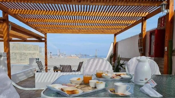 Un espace extérieur abrité, aménagé pour prendre les repas, avec une table dressée pour le petit-déjeuner, des chaises et une vue sur la mer.