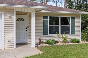 A single-story house with a front door, a small porch, and a window with shutters.