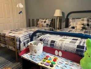 A child's bedroom with two beds, a toy train set, and a basket with a face design.