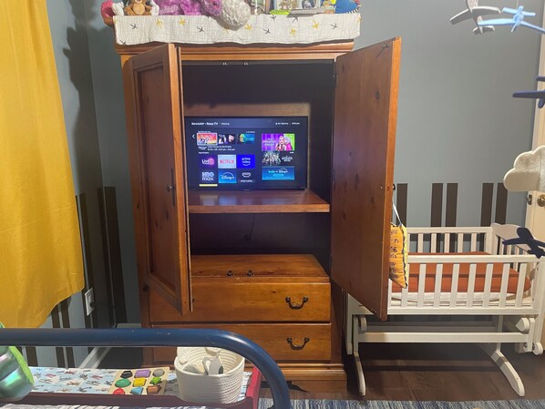 A room with a wooden cabinet containing a television, a crib, and a toy cart.