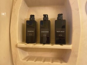 Three black bottles of shampoo, conditioner, and body wash on a white shelf in a bathroom.