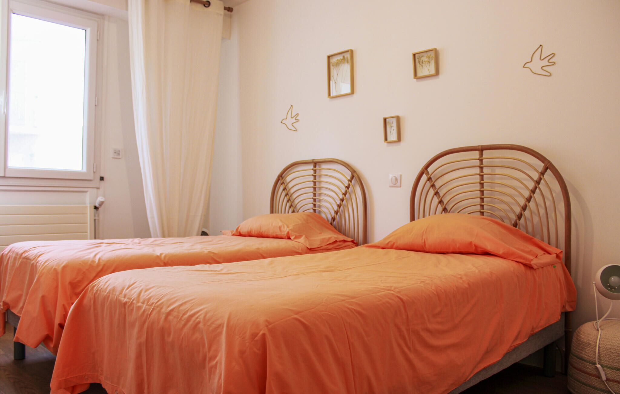 Ein Zimmer mit zwei Betten, einem fensterbelaubten Fenster und Bildern an der Wand.